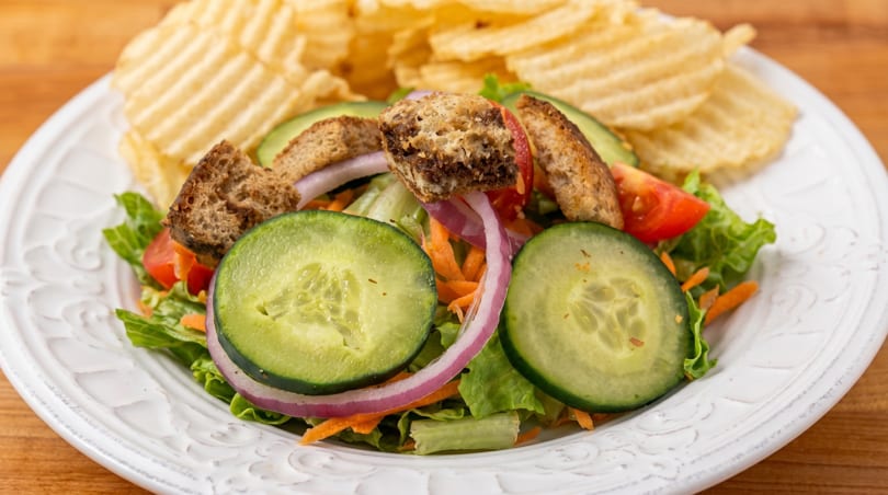 Fresh garden salad with cucumbers, tomatoes, red onion, croutons, and a side of potato chips.