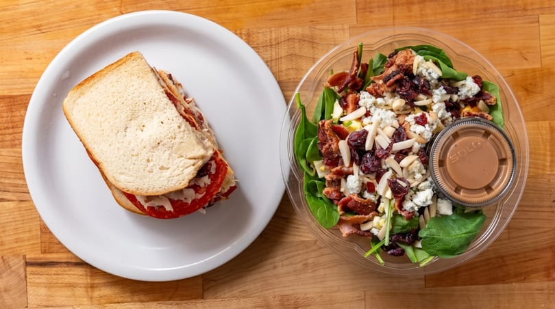 A sandwich on white bread and a salad with spinach, bacon, cranberries, and almonds.